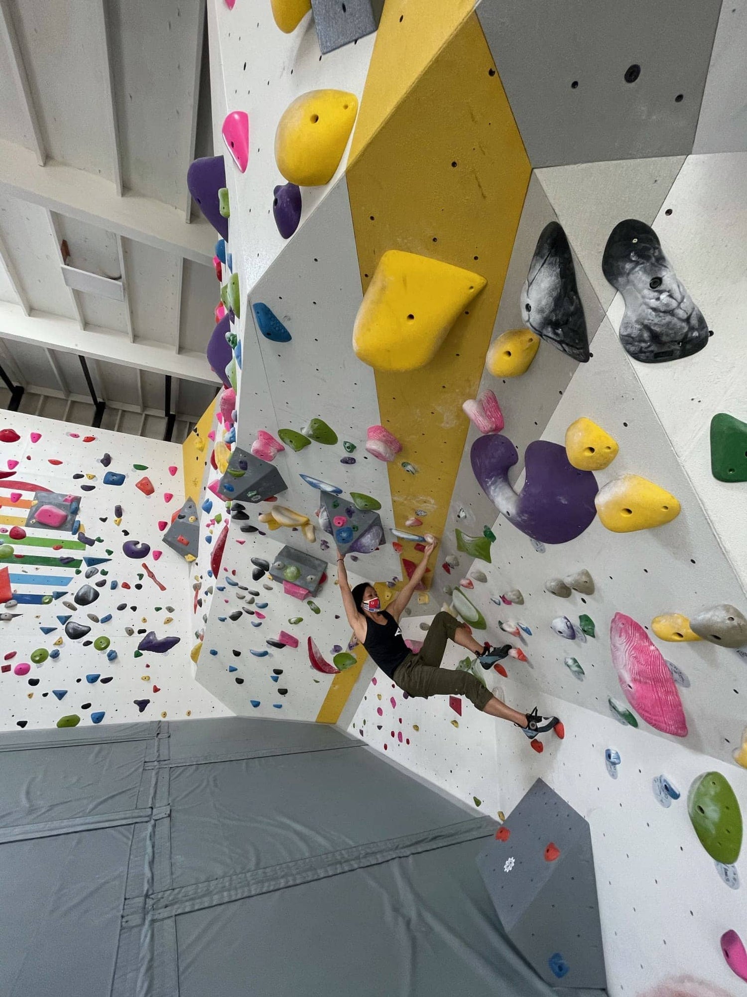 Woman rock climbing on a bouldering wall in a climbing gym, with padded flooring. 