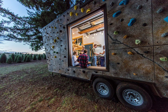 A rock climbing wall on the outside of a tiny home trailer.